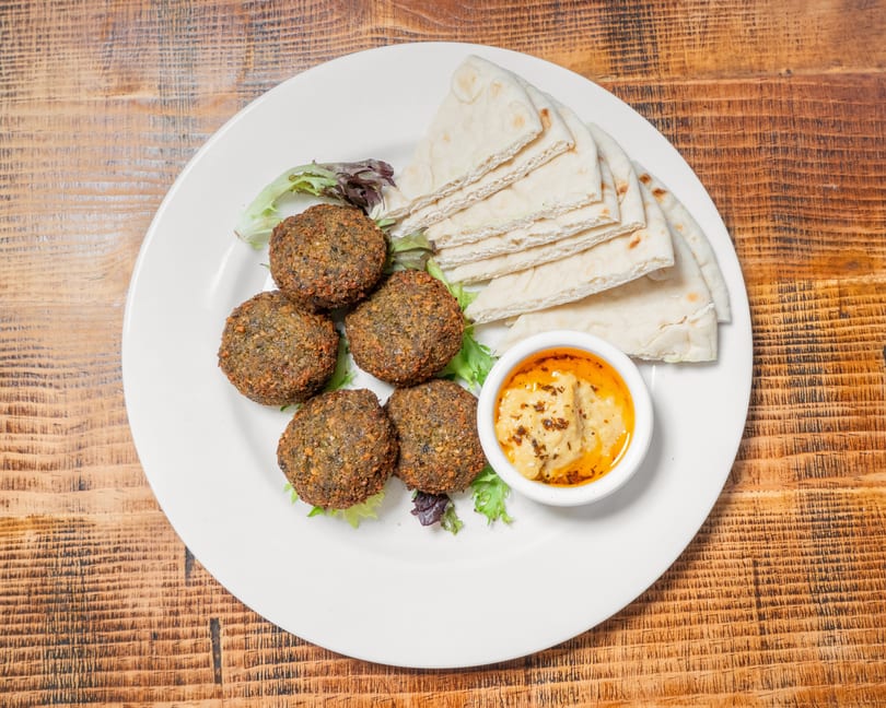 Falafel plate with five falafel balls, pita bread, hummus, and a bed of lettuce.