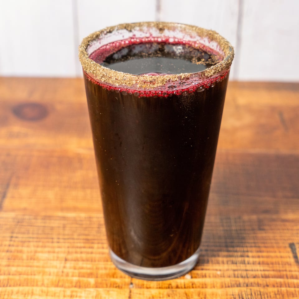 Dark red beverage in a glass with a golden-brown sugar rim, on a wooden table.