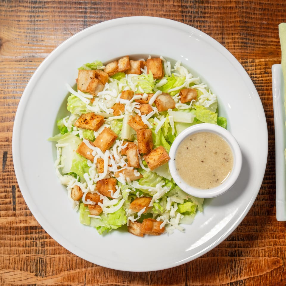Overhead view of a Caesar salad with croutons, shredded cheese, and dressing on a wooden table.