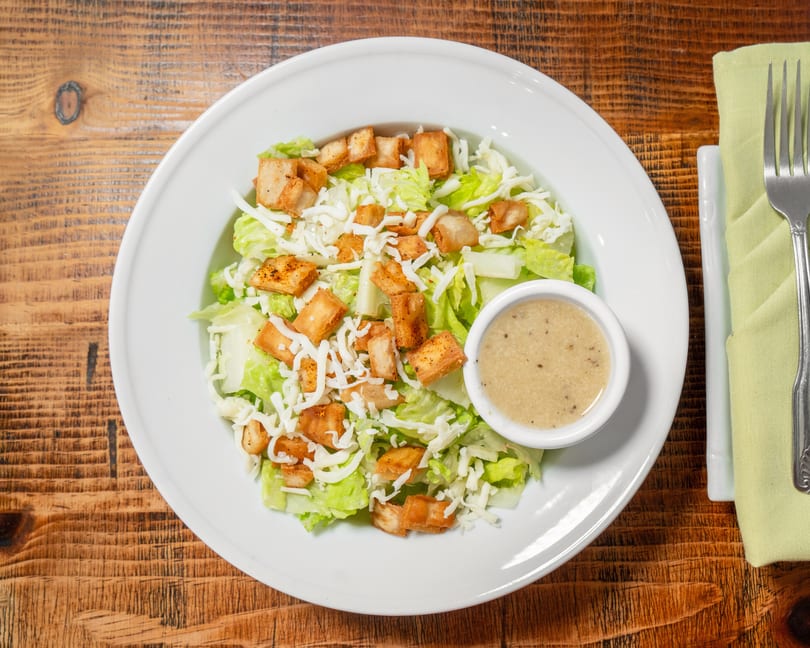 Overhead view of a Caesar salad with croutons, shredded cheese, and dressing on a wooden table.