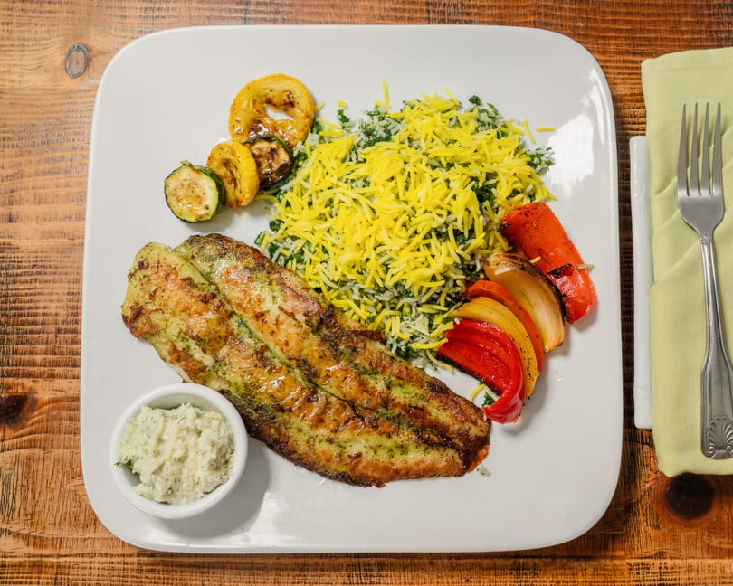 Grilled fish fillet with yellow rice, roasted vegetables, and a side of white sauce on a plate.
