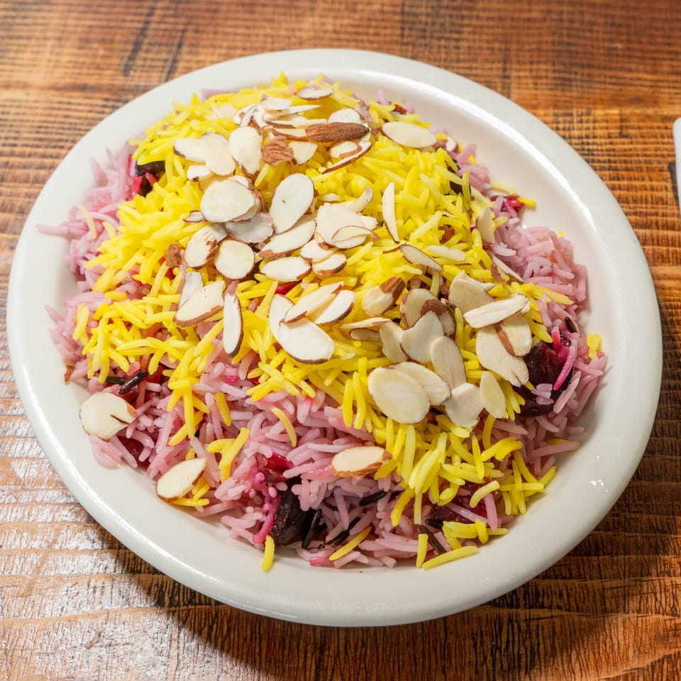Colorful rice pilaf with yellow, pink, and dark grains, topped with sliced almonds on a white plate.