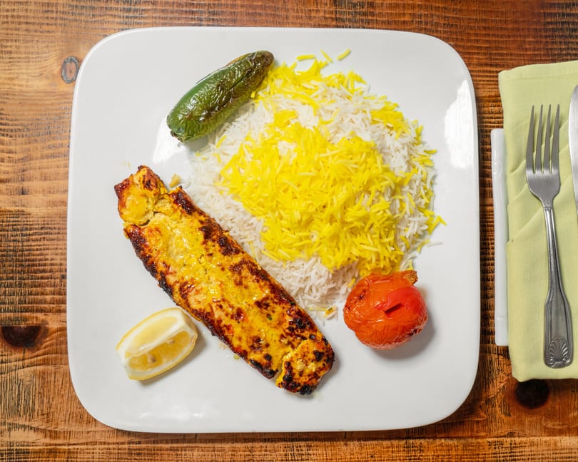 Grilled chicken, white and yellow rice, roasted tomato, and green pepper on a white plate.