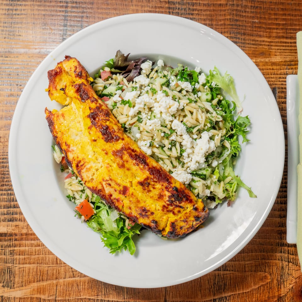 Grilled chicken breast with a side of orzo pasta salad, feta, and greens on a white plate.