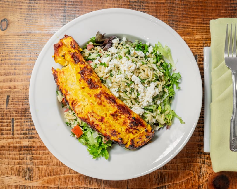 Grilled chicken breast with a side of orzo pasta salad, feta, and greens on a white plate.
