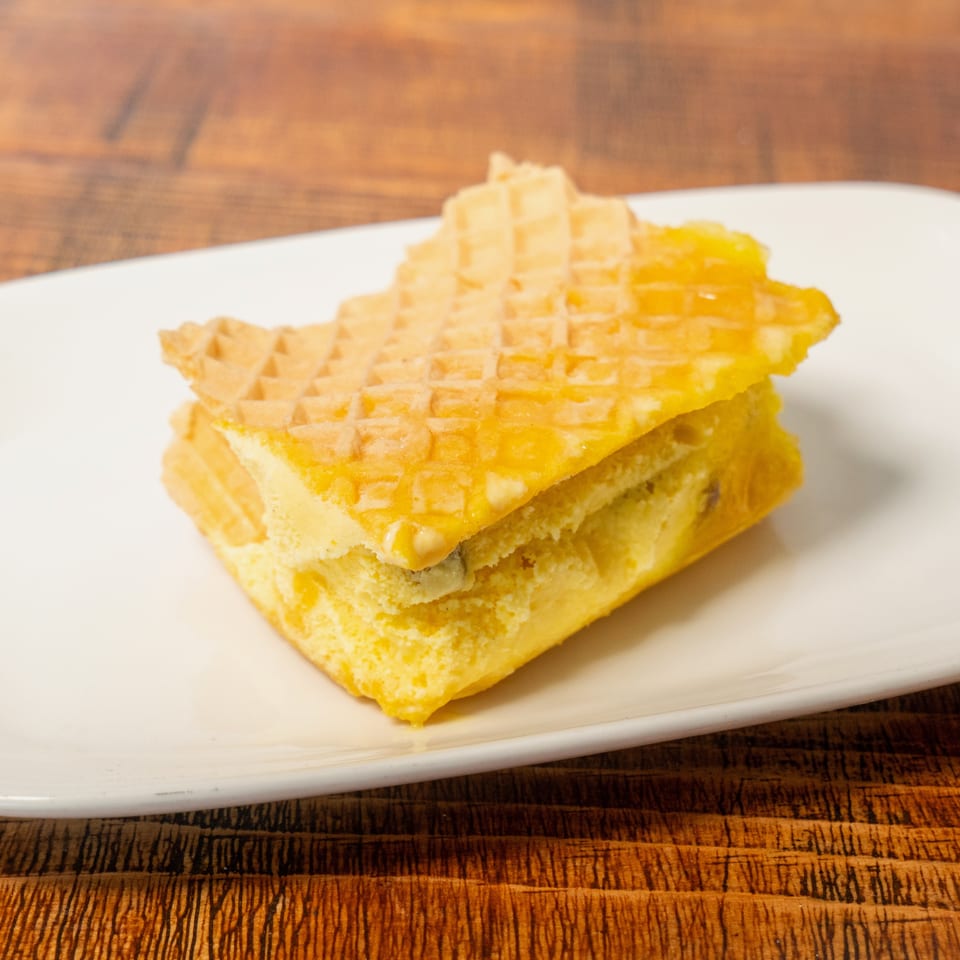 A yellow dessert bar with a waffle-like top and creamy filling on a white plate.