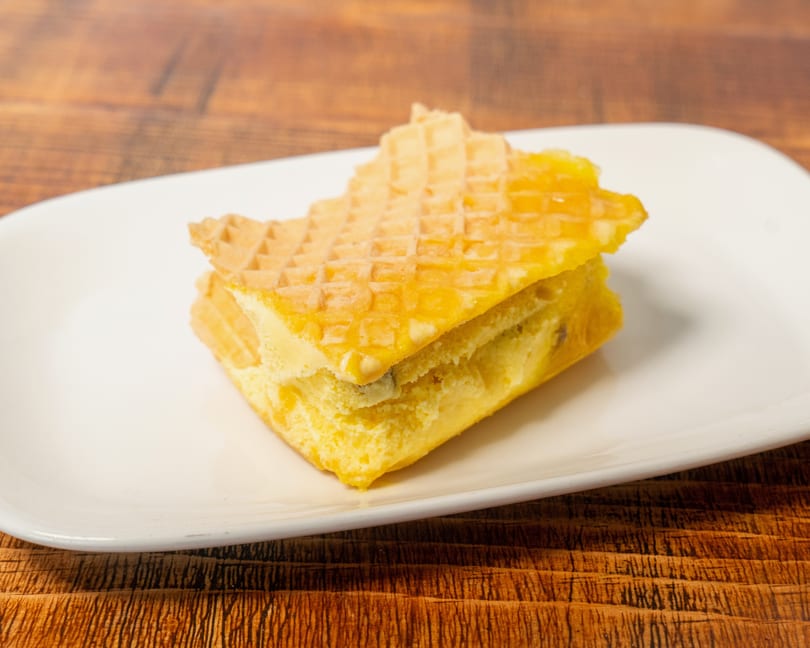A yellow dessert bar with a waffle-like top and creamy filling on a white plate.