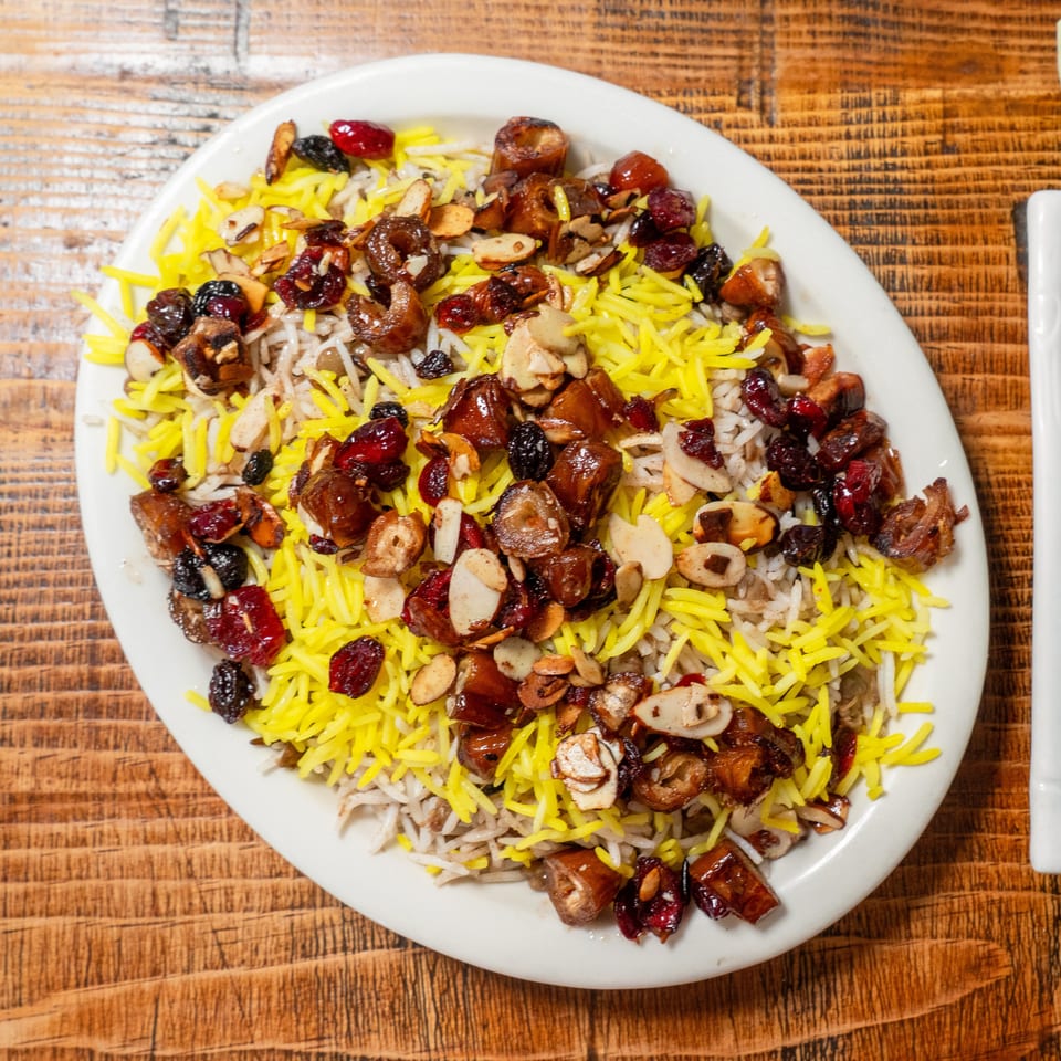 Colorful rice dish with yellow saffron rice, dates, cranberries, and sliced almonds on a white plate.