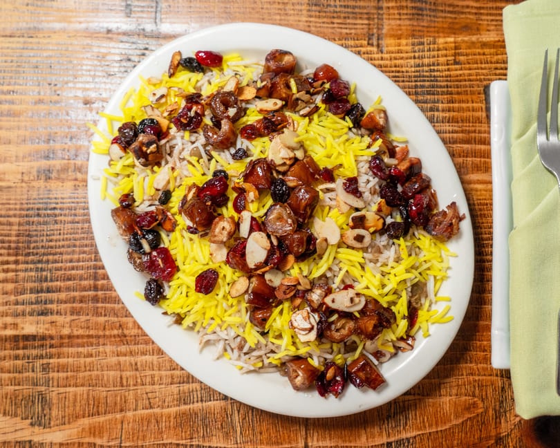 Colorful rice dish with yellow saffron rice, dates, cranberries, and sliced almonds on a white plate.