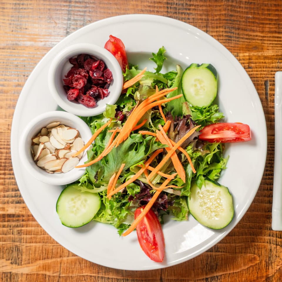 A fresh garden salad with mixed greens, cucumbers, tomatoes, shredded carrots, cranberries, and almonds.