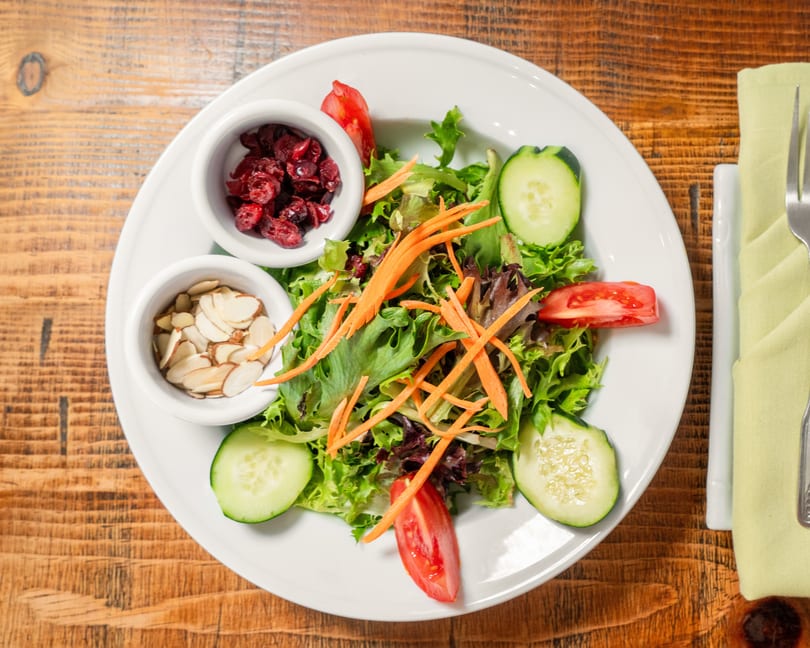 A fresh garden salad with mixed greens, cucumbers, tomatoes, shredded carrots, cranberries, and almonds.