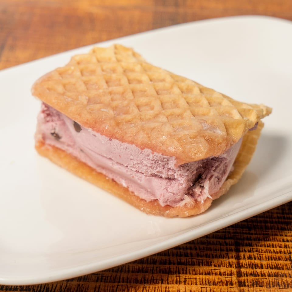 A waffle ice cream sandwich with purple ice cream and chocolate chips on a white plate.