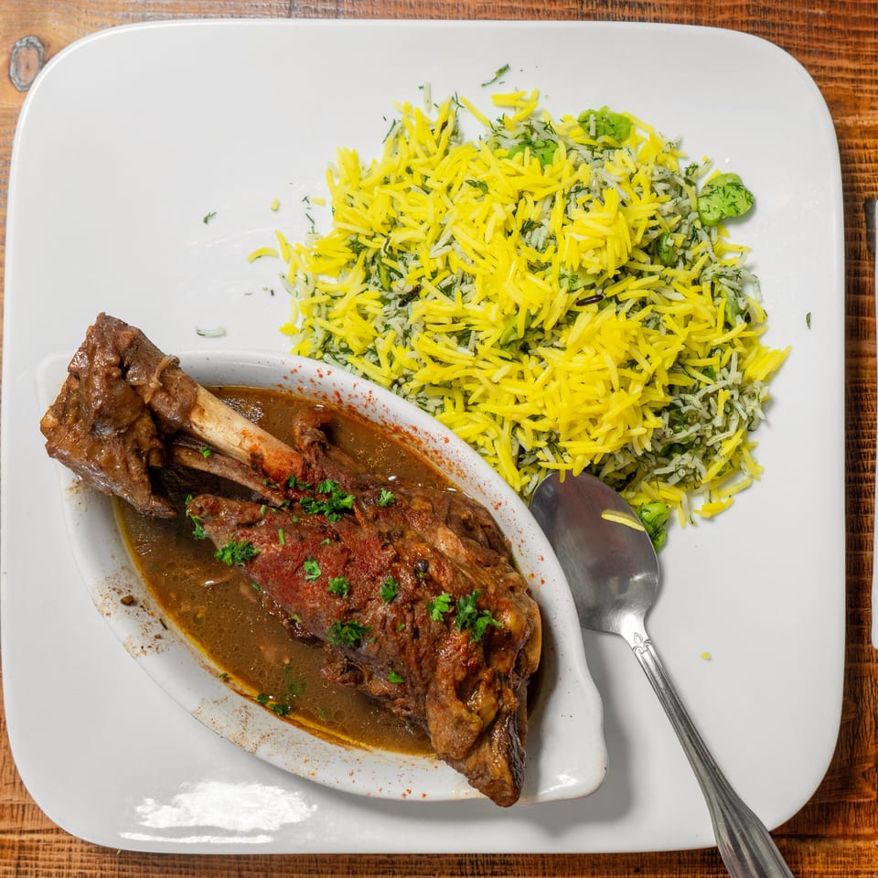 Braised lamb shank with a rich sauce and a side of yellow and green herb rice.
