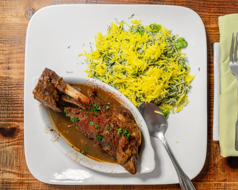 Braised lamb shank with a rich sauce and a side of yellow and green herb rice.