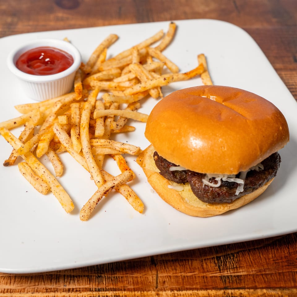 A burger with shredded cheese and a side of seasoned fries with ketchup on a white plate.