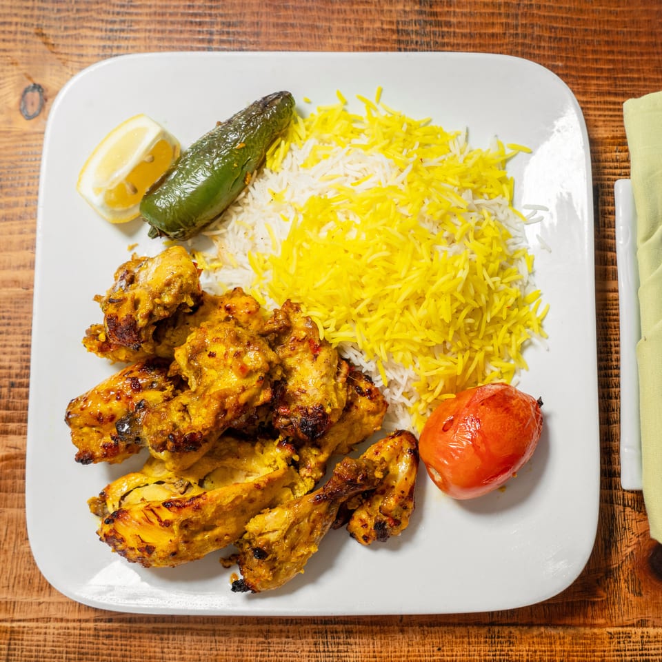 Chicken kabob with saffron rice, grilled tomato, jalapeno, and lemon on a white plate.