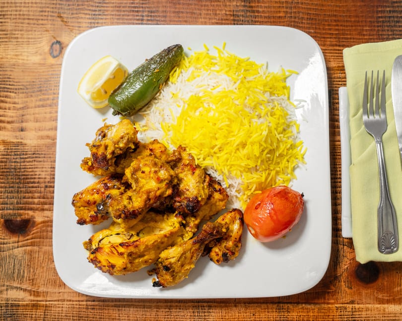 Chicken kabob with saffron rice, grilled tomato, jalapeno, and lemon on a white plate.