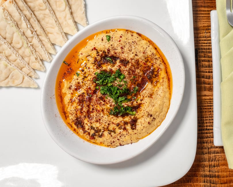 Hummus topped with paprika, olive oil, and parsley, served with pita bread.