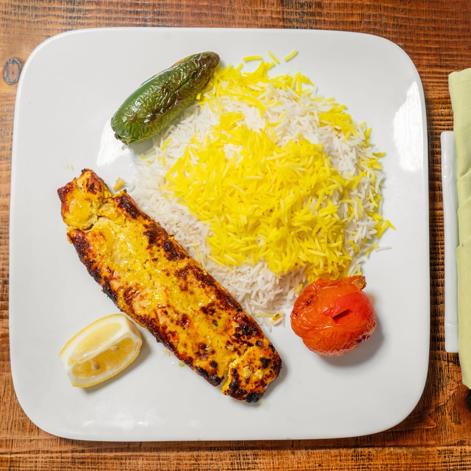 Grilled chicken kebab with saffron rice, roasted tomato, and jalapeño on a white plate.