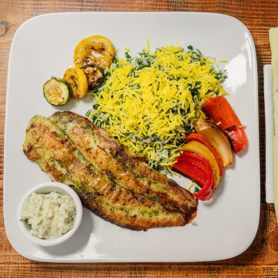 Grilled fish with yellow rice, roasted zucchini, and bell peppers on a white plate.