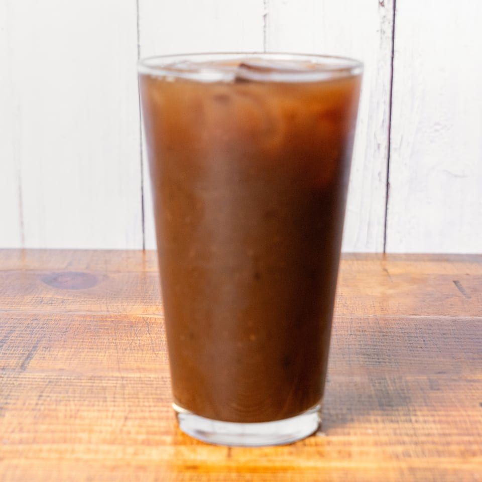Iced coffee in a tall glass with ice cubes on a wooden table.