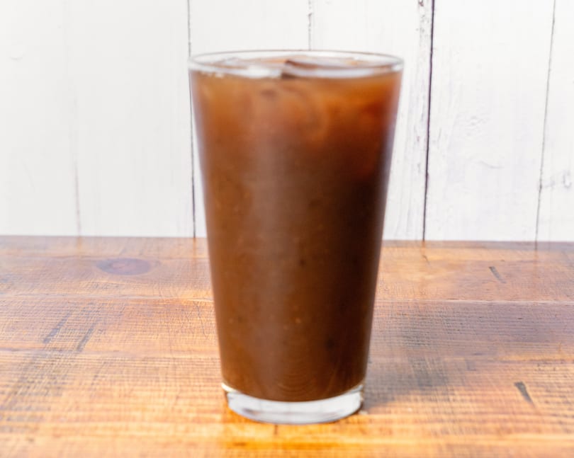 Iced coffee in a tall glass with ice cubes on a wooden table.