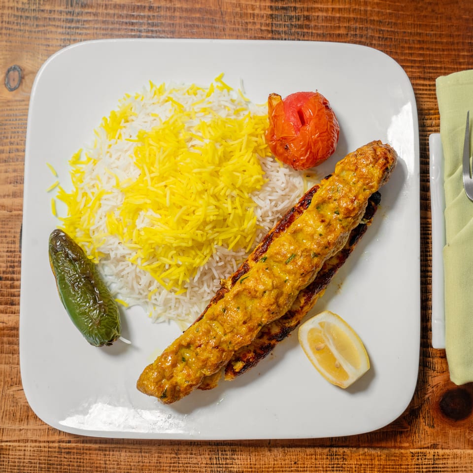 Chicken koobideh with saffron rice, grilled tomato, and jalapeño on a white plate.