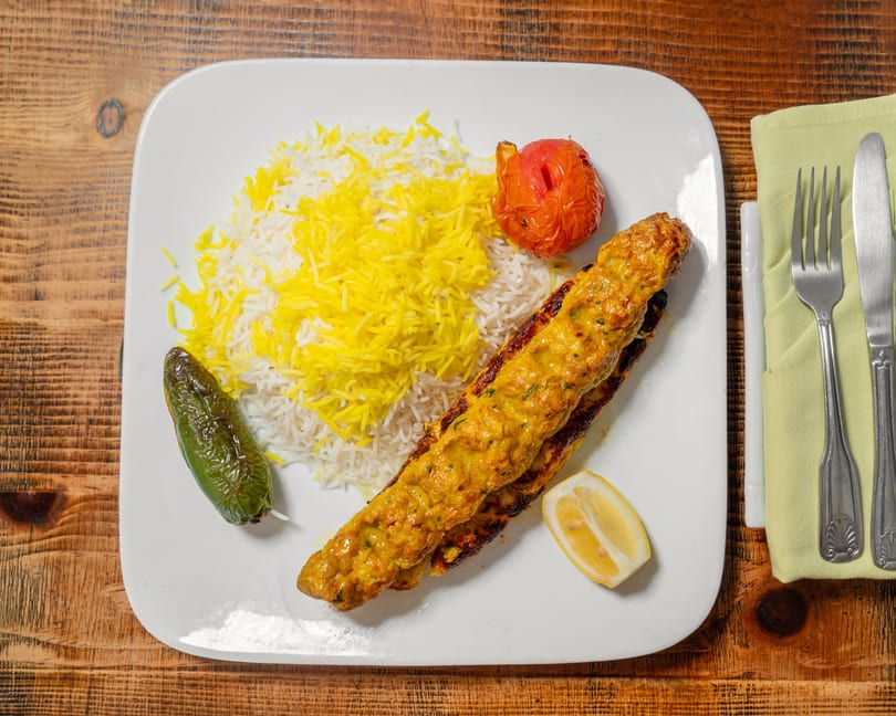 Chicken koobideh with saffron rice, grilled tomato, and jalapeño on a white plate.