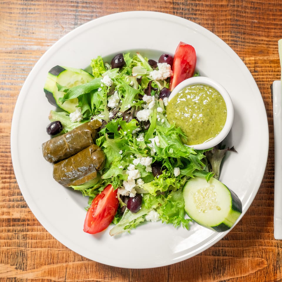 A fresh Greek salad with dolmades, feta, olives, tomatoes, cucumbers, and green dressing.