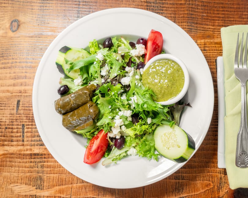 A fresh Greek salad with dolmades, feta, olives, tomatoes, cucumbers, and green dressing.