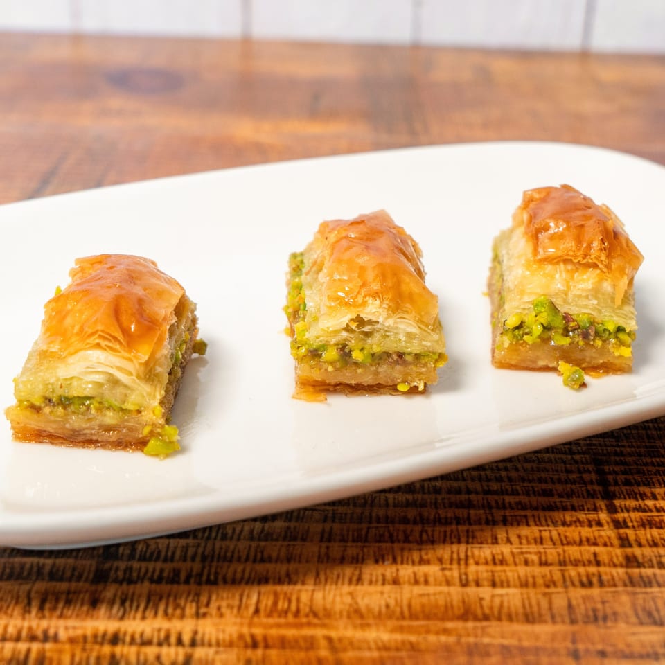 Three pieces of golden baklava with green pistachio filling on a white rectangular plate.