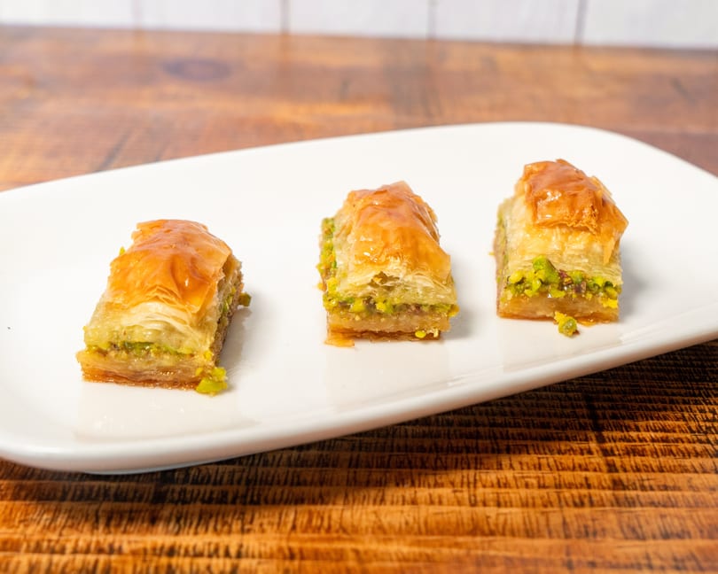Three pieces of golden baklava with green pistachio filling on a white rectangular plate.