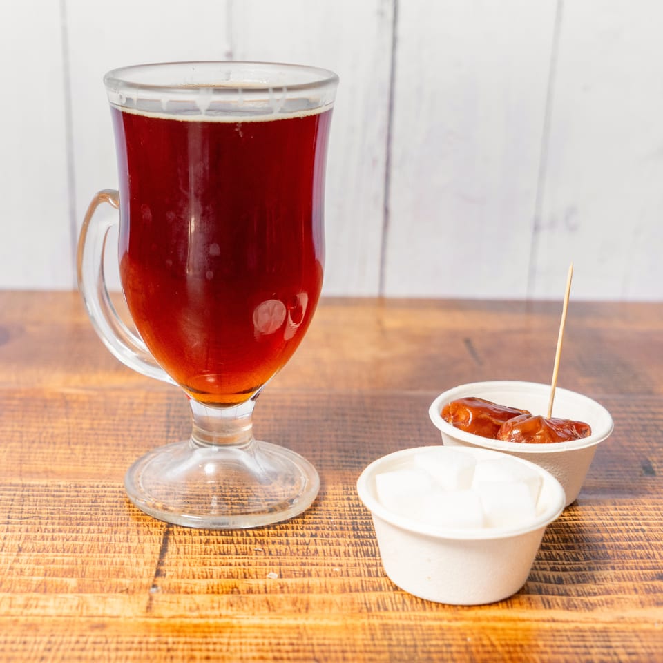 A glass of dark tea, with small cups of dates and sugar cubes on a wooden table.