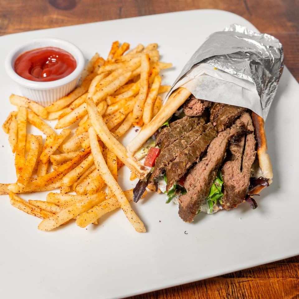 Gyro sandwich with sliced meat, lettuce, and tomatoes, served with seasoned fries and ketchup.