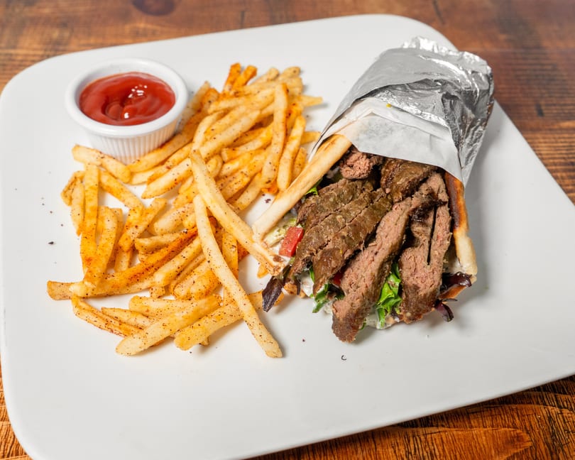 Gyro sandwich with sliced meat, lettuce, and tomatoes, served with seasoned fries and ketchup.