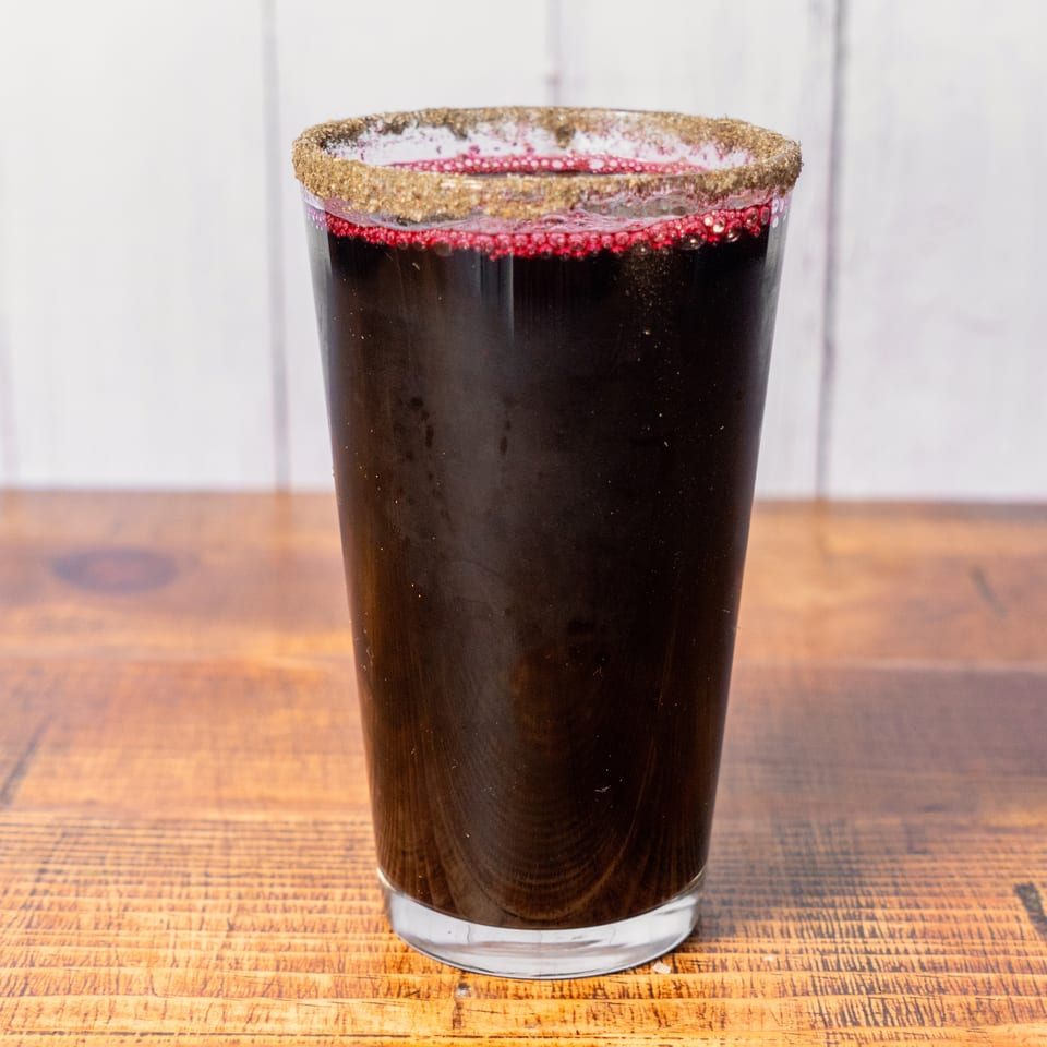 A dark red drink in a glass with a spiced rim, on a wooden table.