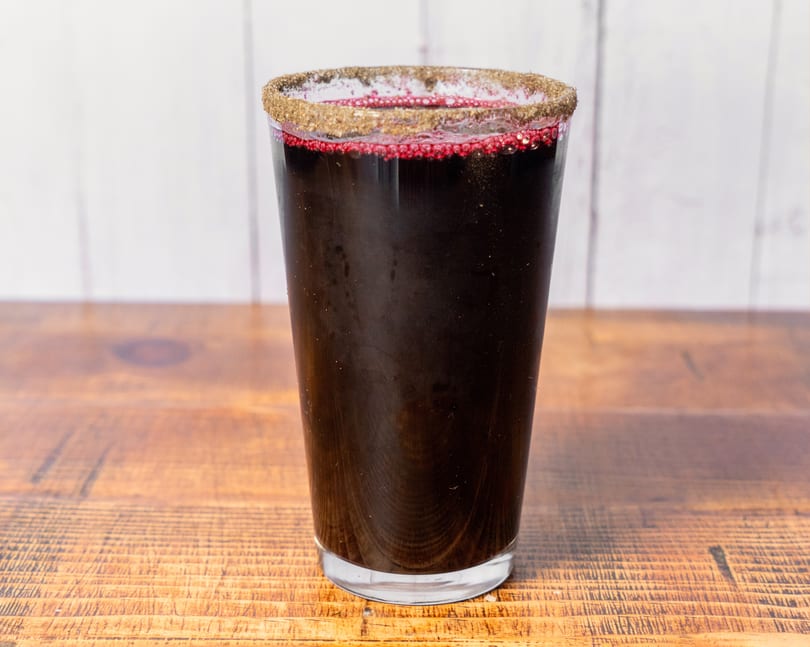 A dark red drink in a glass with a spiced rim, on a wooden table.